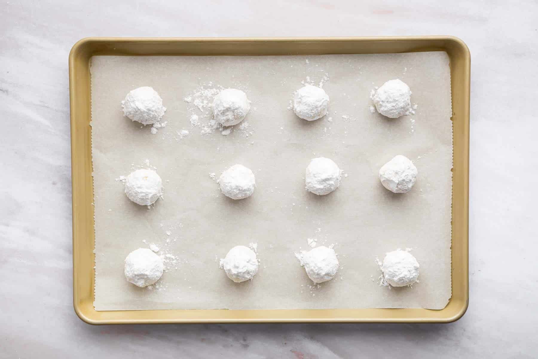Twelve powdery white cookies in a baking sheet.
