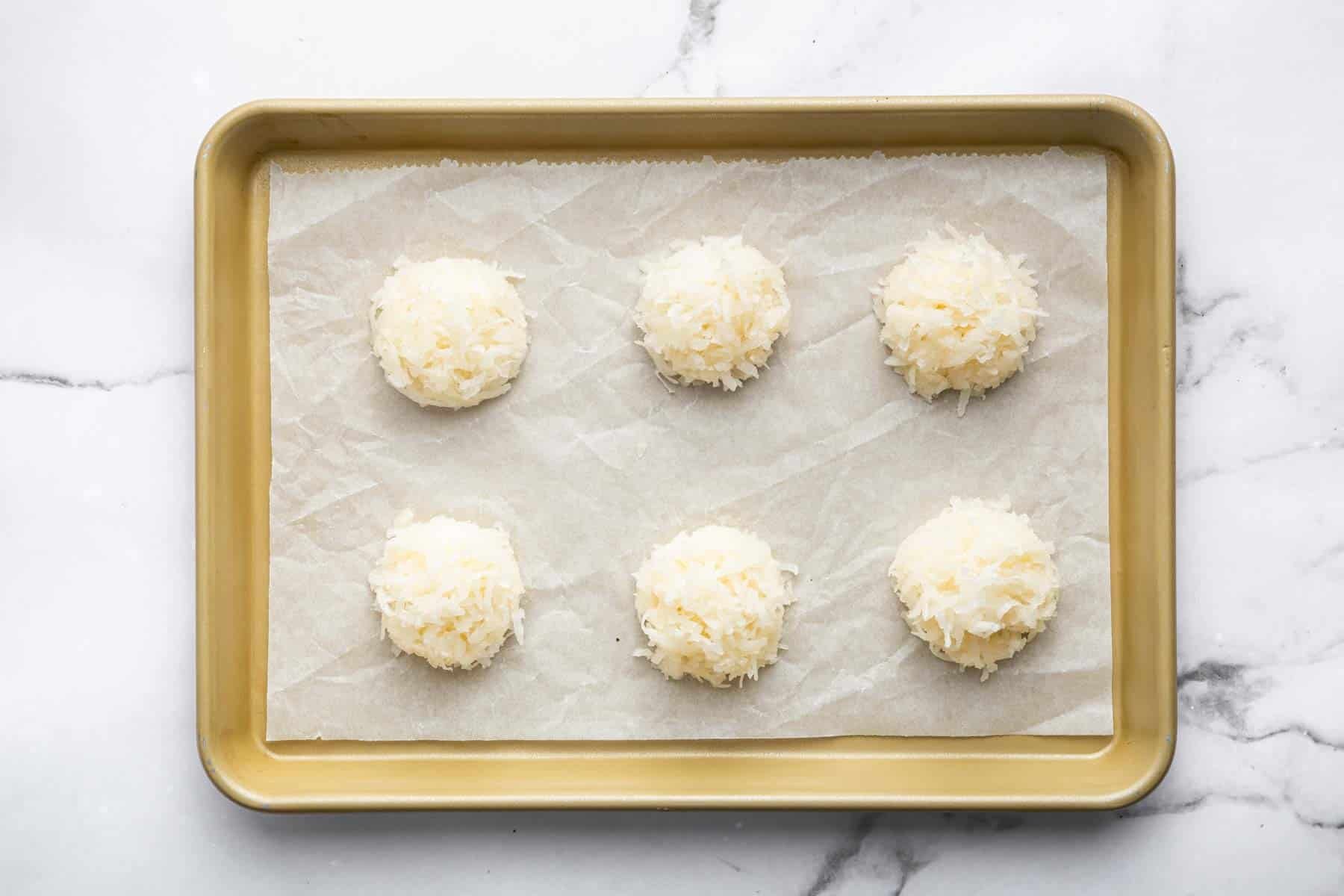 Six white cookies on a baking sheet lined with parchment paper.