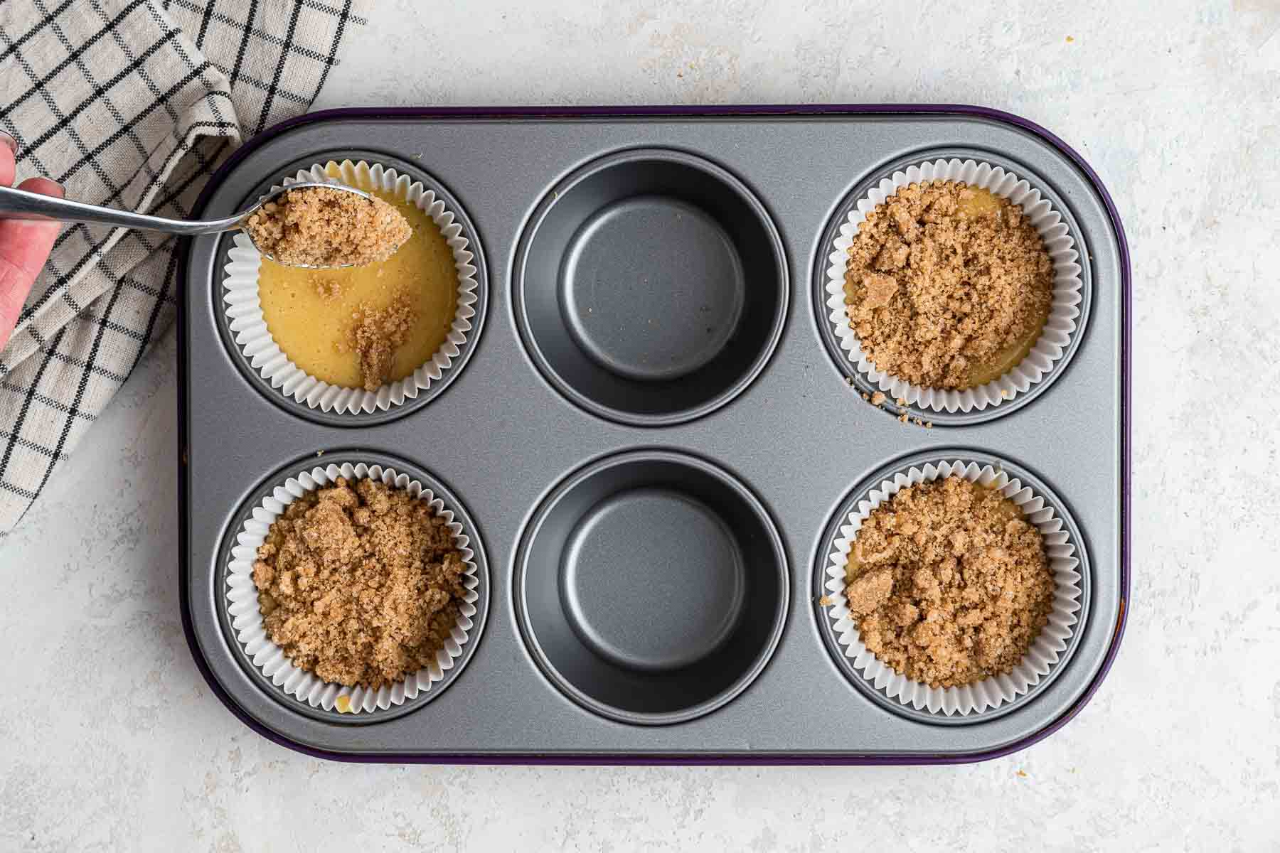 Adding crumb topping in a muffin pan before baking.