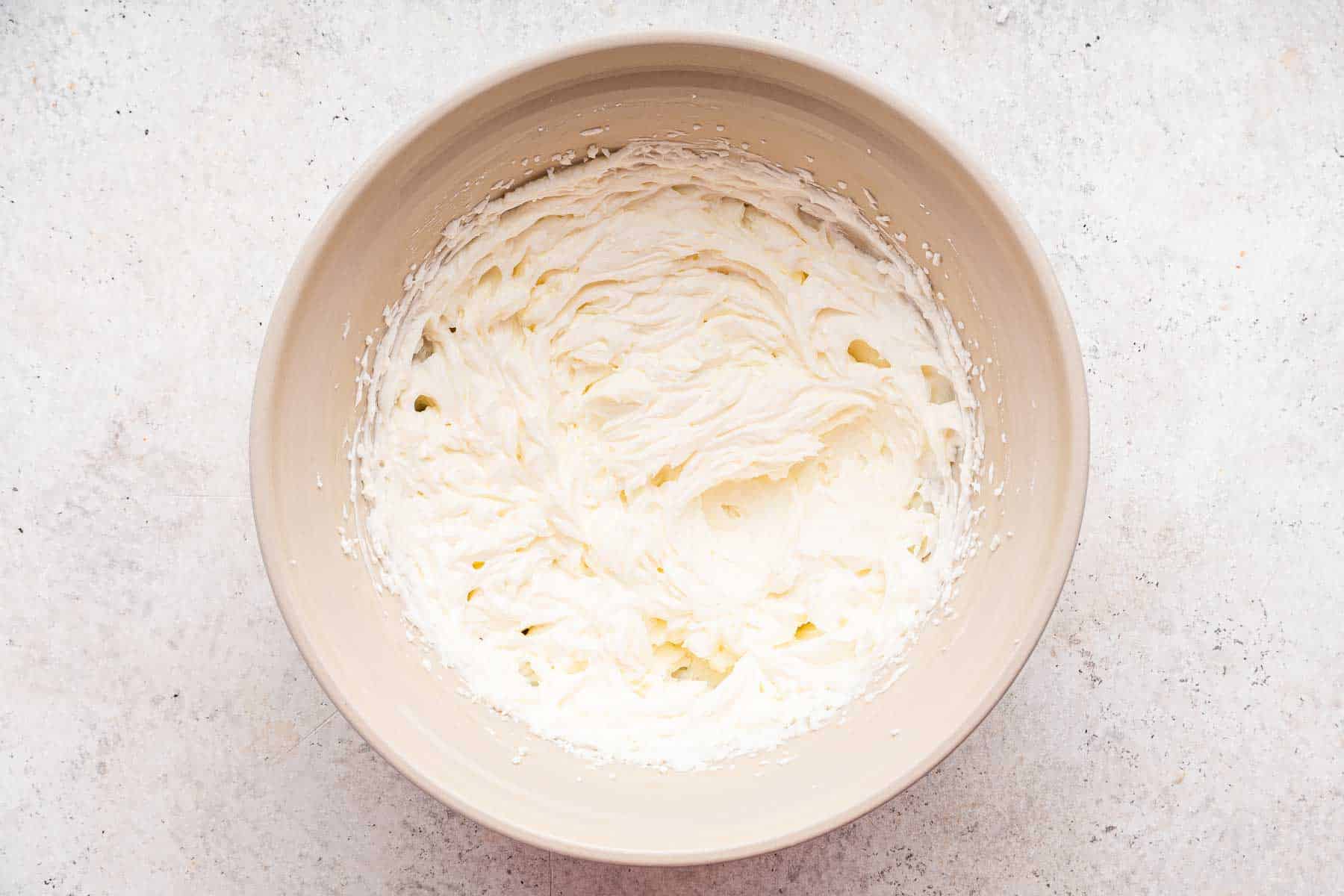 Brown bowl of beaten cream cheese and sugar.