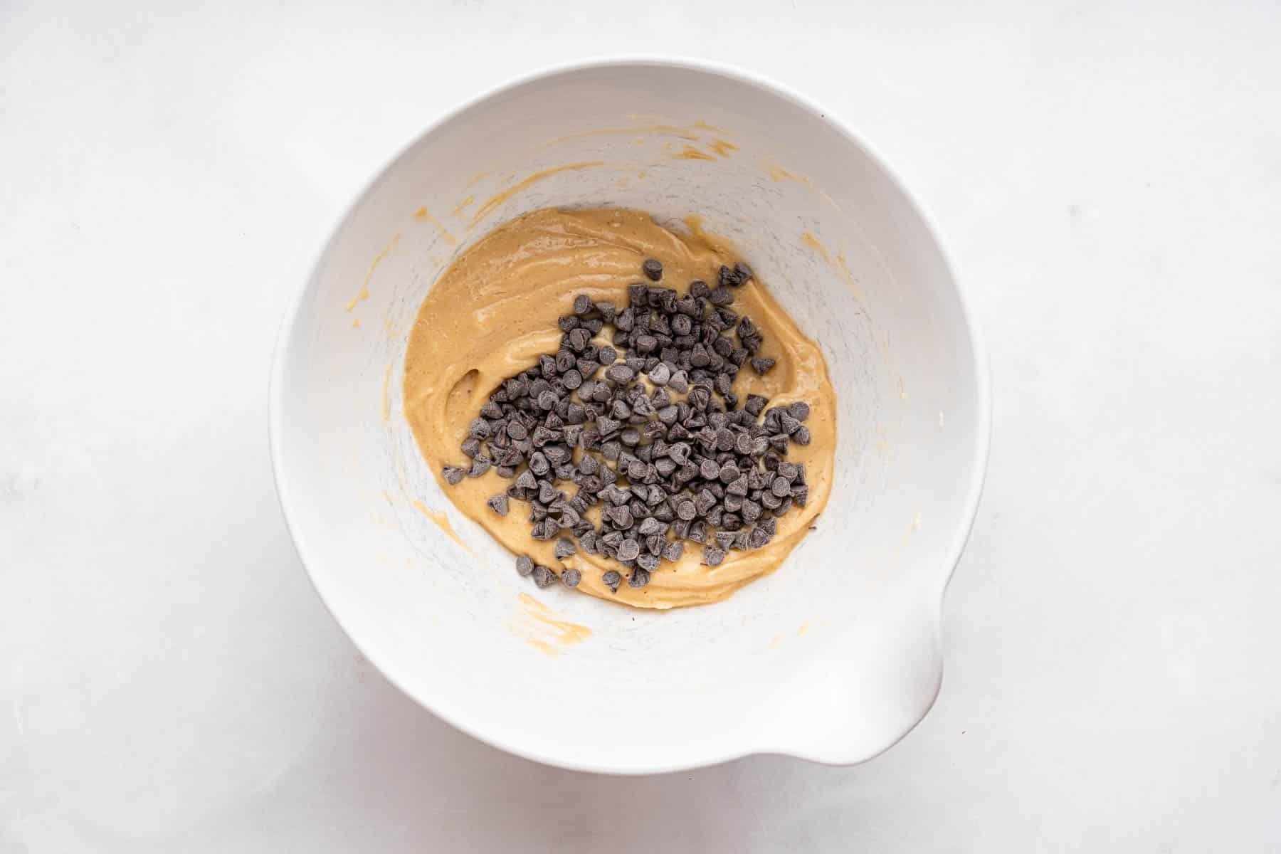 Chocolate chips on top of brown dessert batter in white bowl.