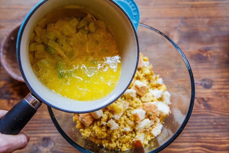 Melted butter and veggies being poured into a bowl with breadcubes.