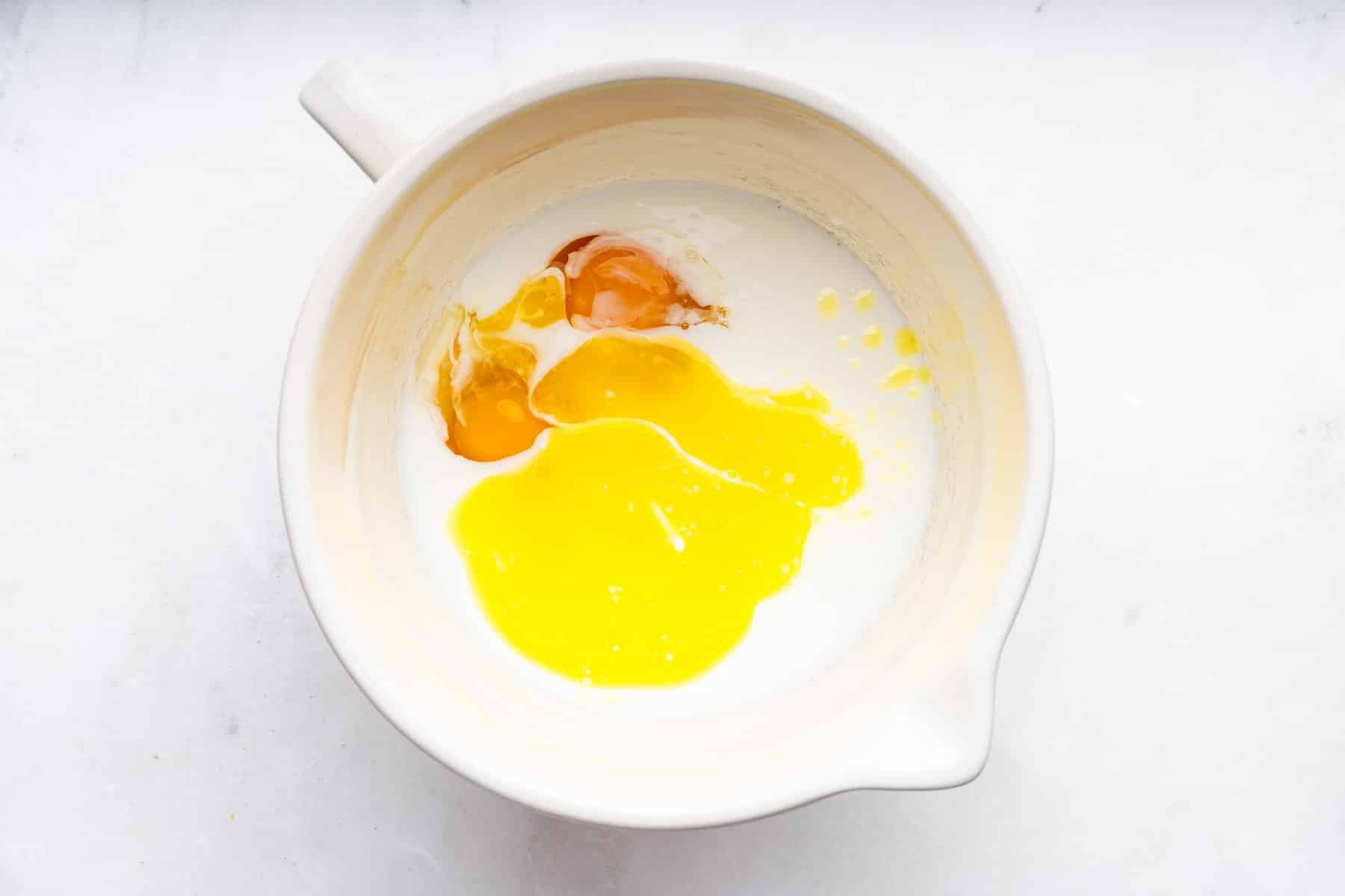 White bowl with melted butter and eggs in white buttermilk.