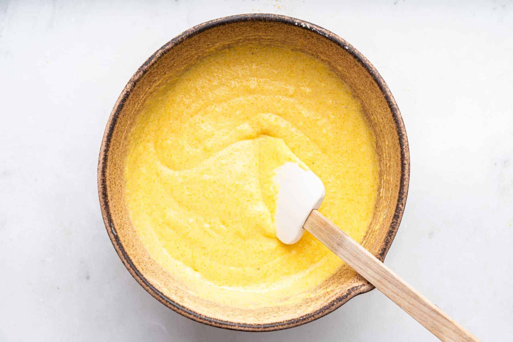 Yellow batter in a brown bowl with white spatula.