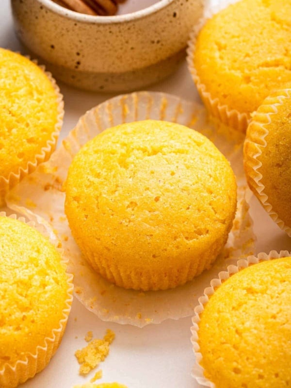Six yellow cornbread muffins on a counter next to honey pot.