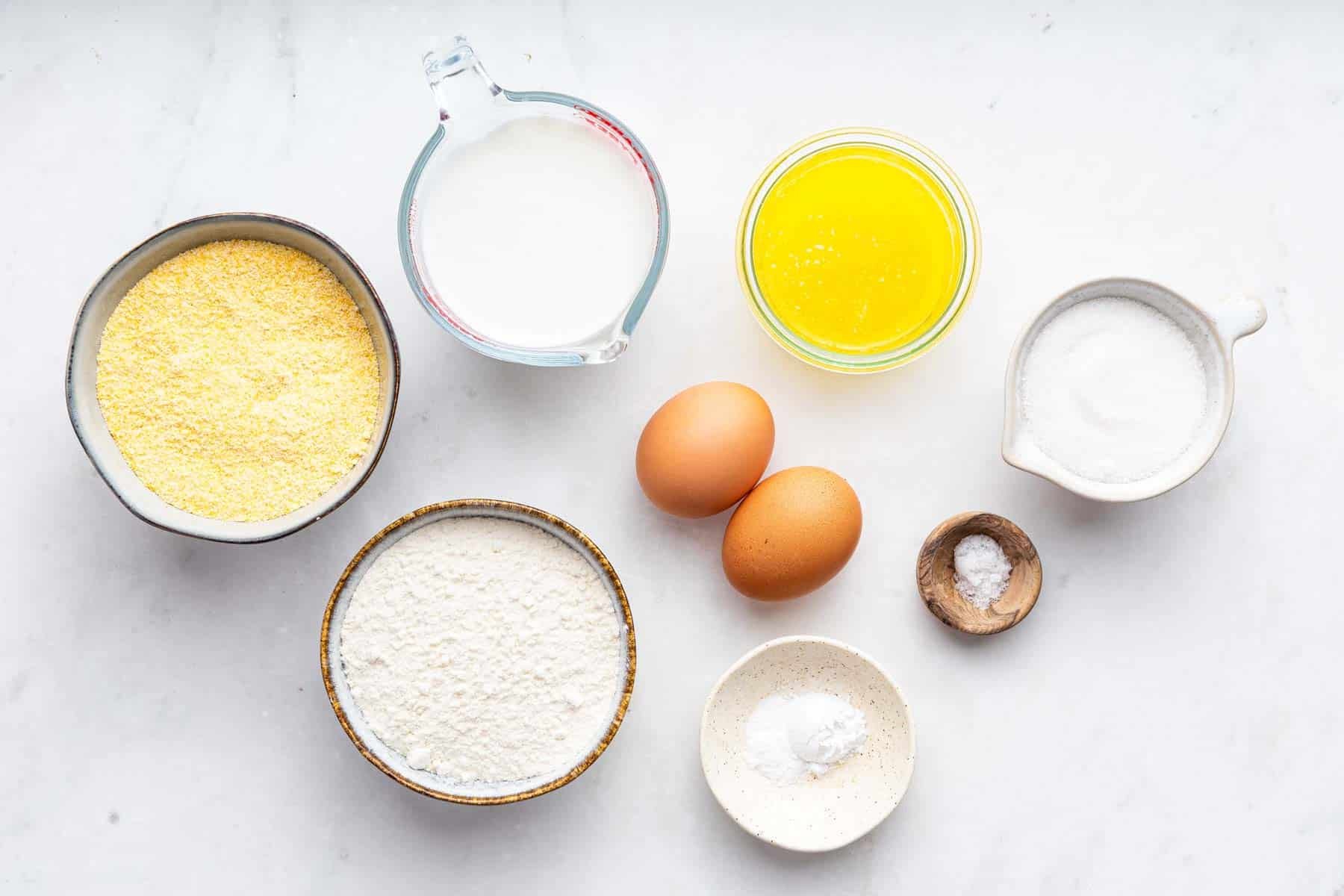 Bowls of white ingredients and two eggs on kitchen counter.
