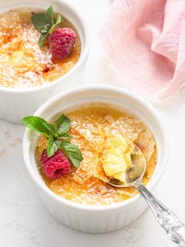 Creme brulee in two ramekins with berries and spoon.