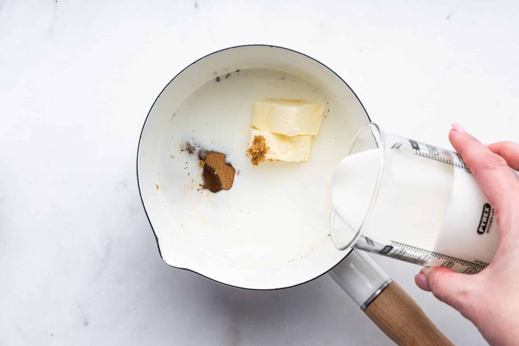 Hand pouring cream into saucepan with butter and brown sugar.