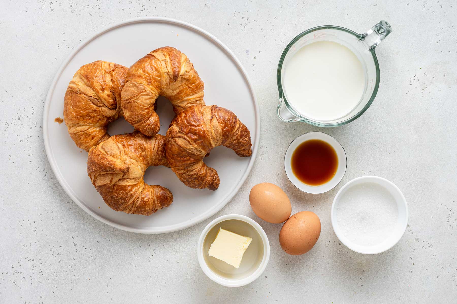 Ingredients for croissant French toast on white table.