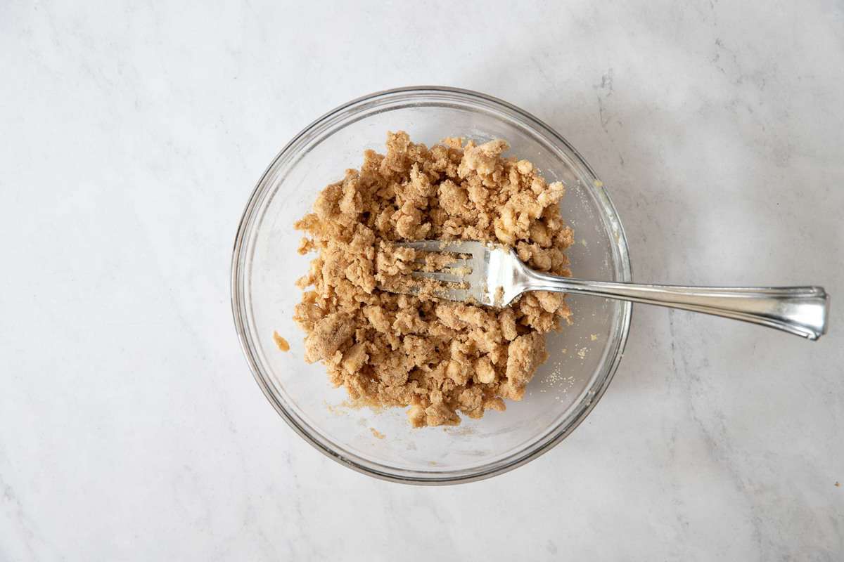Clear bowl of streusel topping on a marble counter.