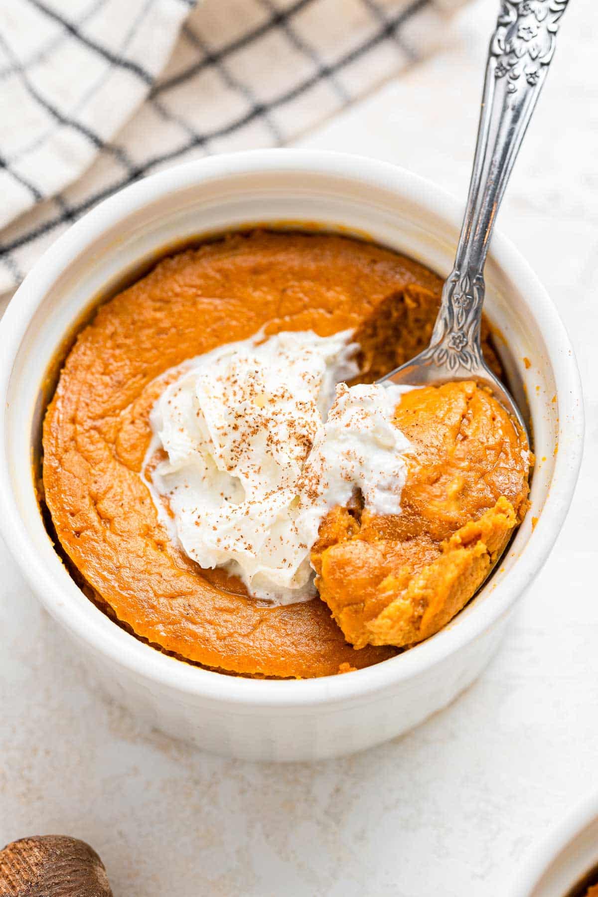 Pumpkin pie in ramekin with melting whipped cream and spoon.