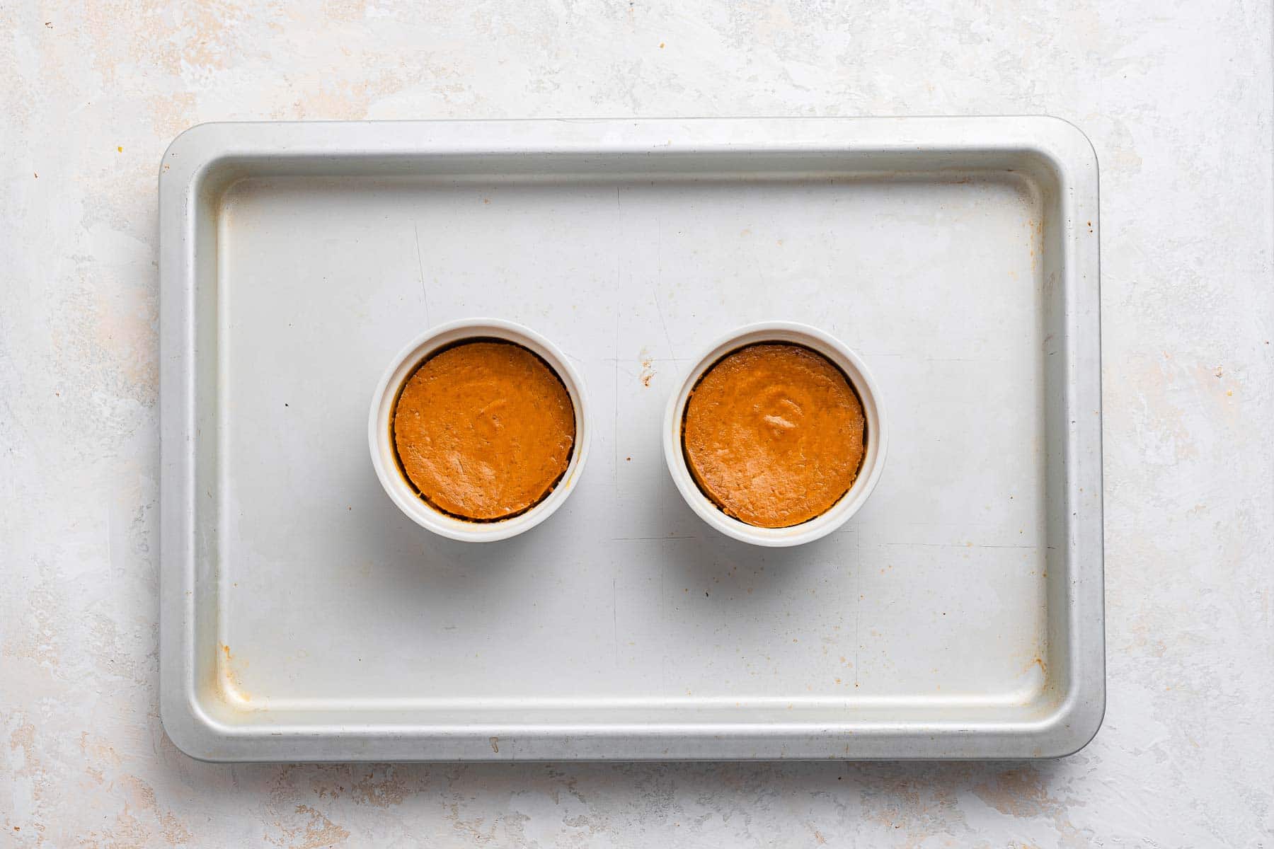 Pumpkin pies in ramekins on baking sheet.
