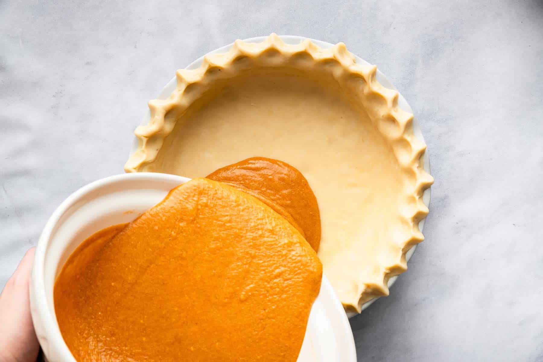 Pouring bright orange batter into a crust on a marble board.