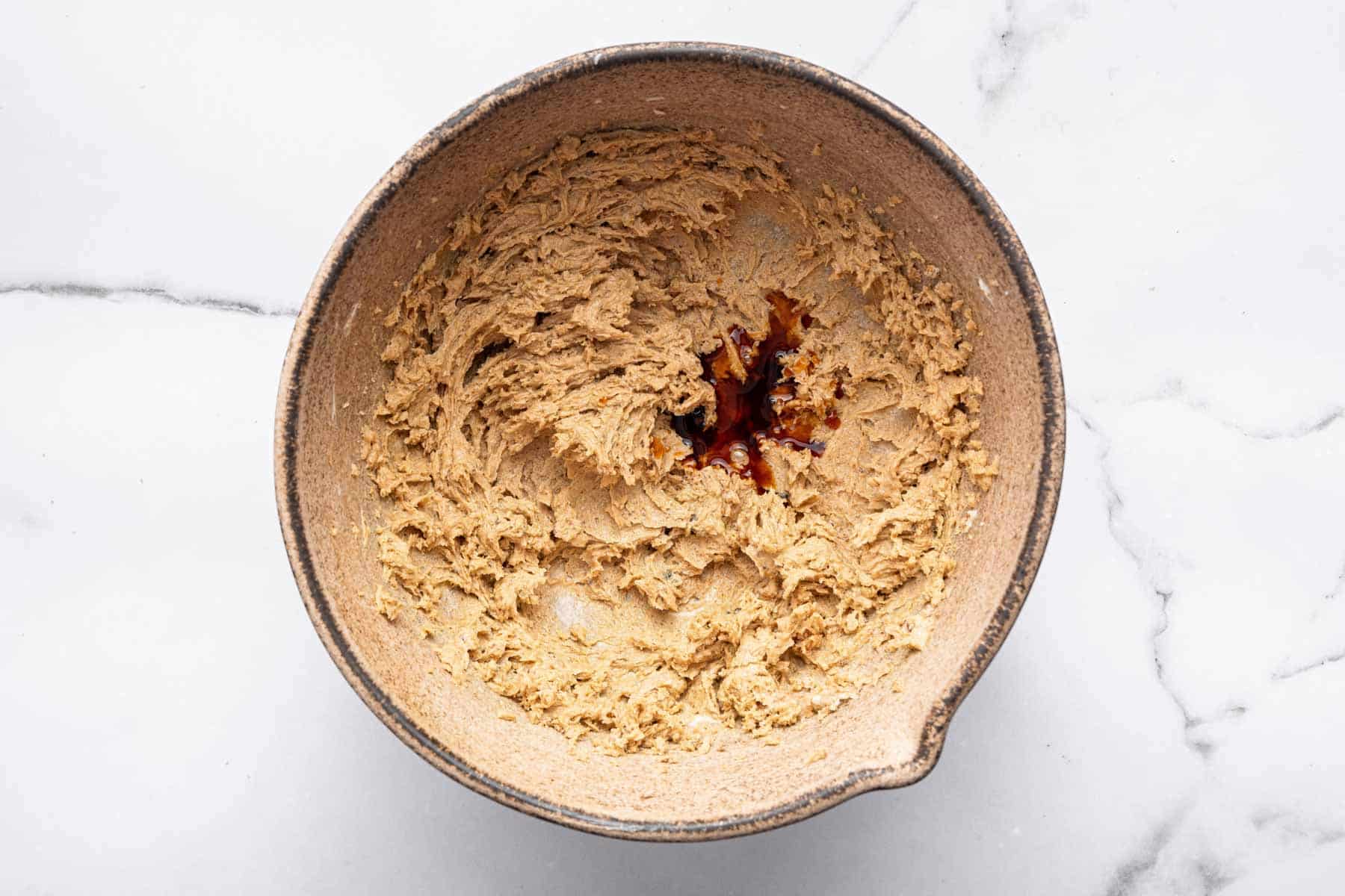 Brown batter in brown bowl with splash of vanilla.