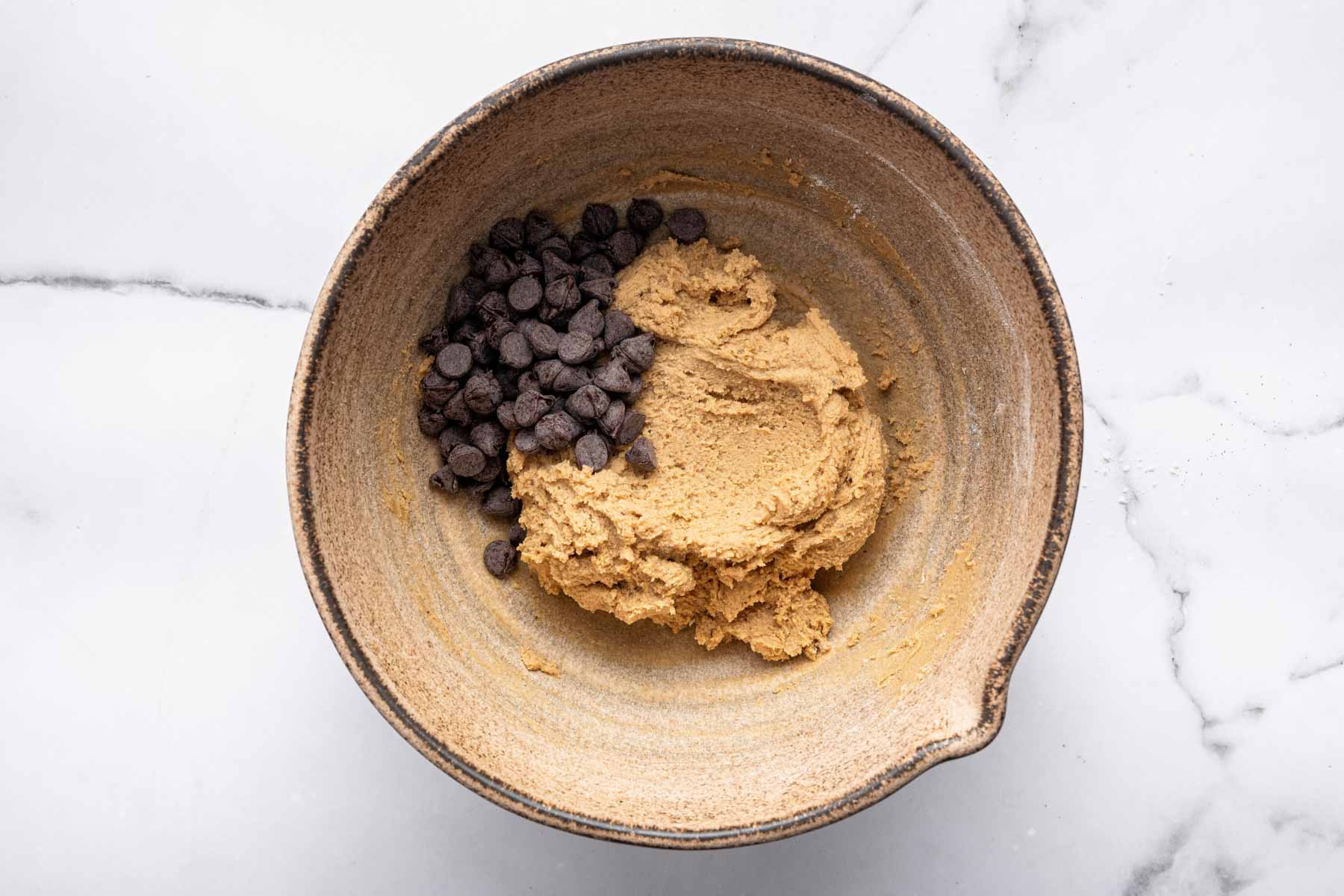 Adding chocolate chips to a brown cookie batter without eggs.