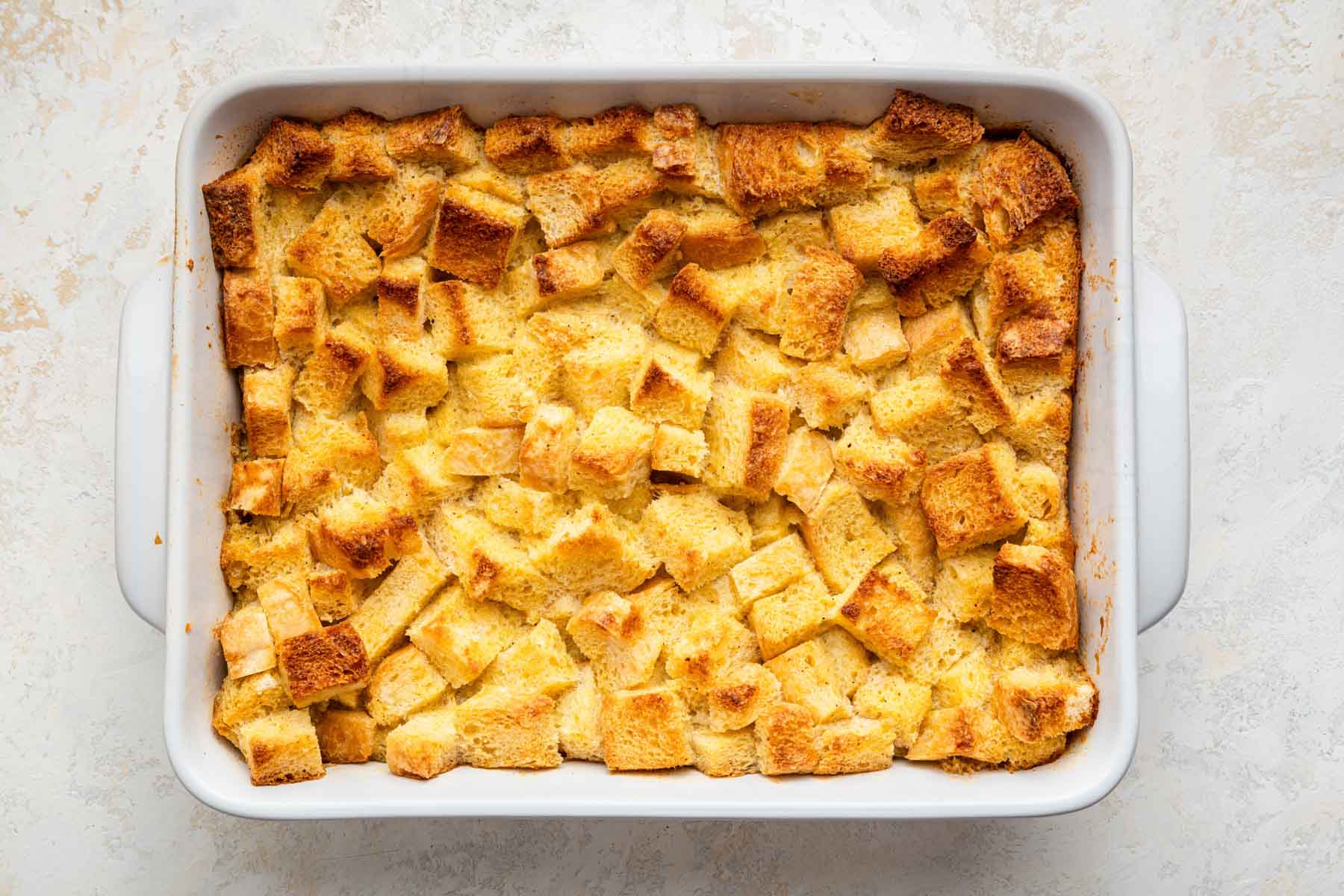 Freshly baked eggnog bread pudding in white rectangular dish.