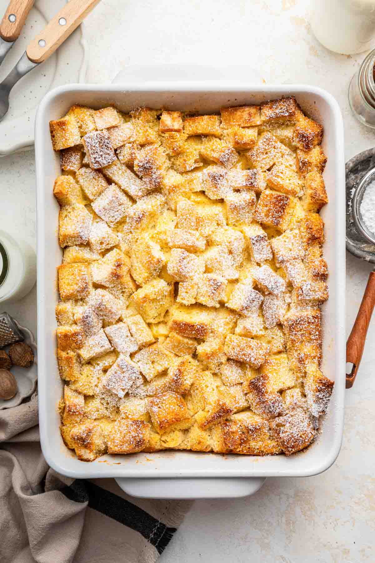 White rectangular dish of eggnog bread pudding dusted with powdered sugar.