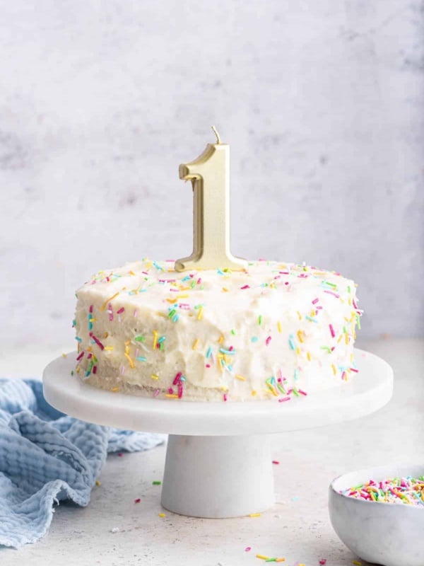 Baby's first birthday cake with white frosting and sprinkles and a candle on top for a smash cake.