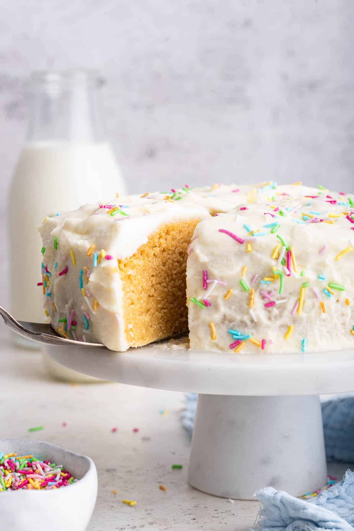 Baby's first birthday cake on white pedestal with sprinkles.