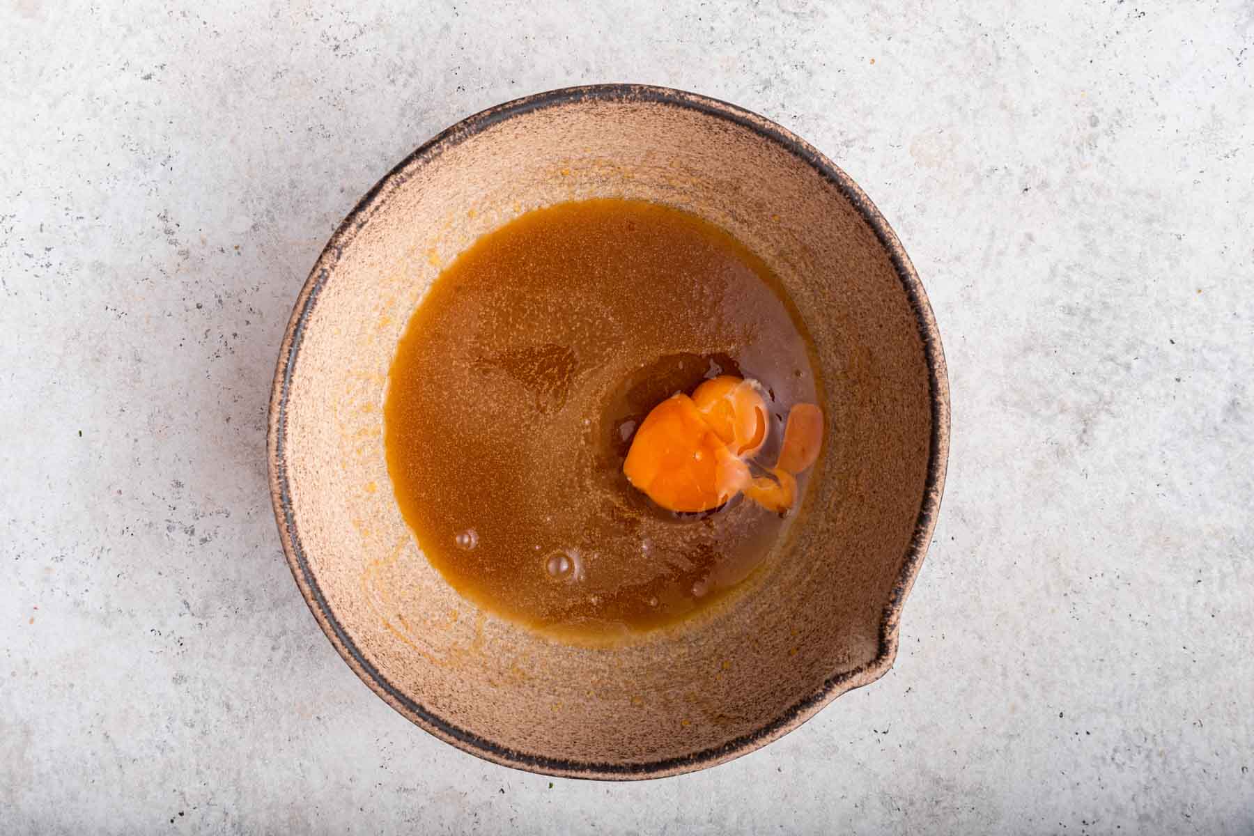 Freshly cracked egg in a bowl with brown cake batter.