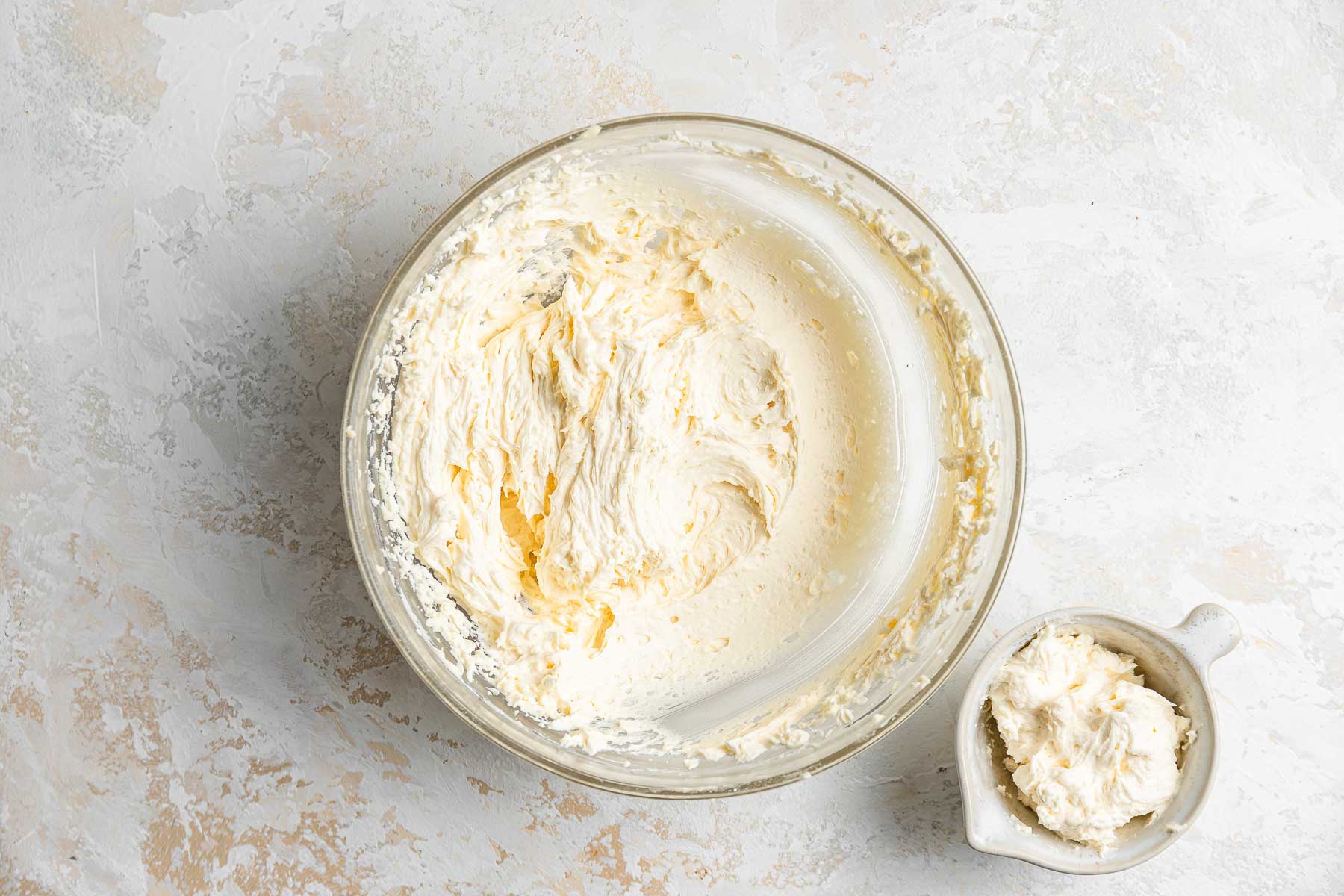 Whipped vanilla buttercream frosting in a clear glass bowl.