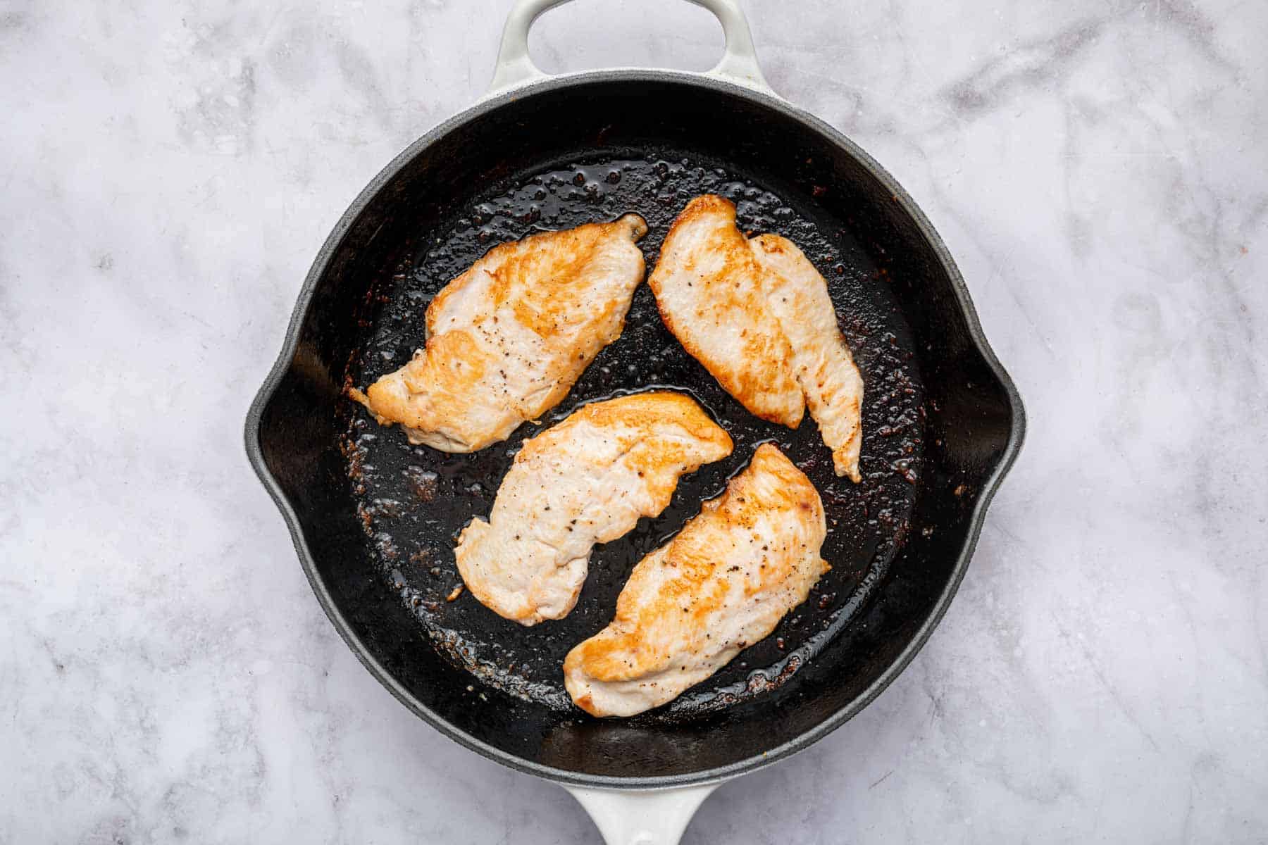 Four thin chicken cutlets in a black cast iron skillet.