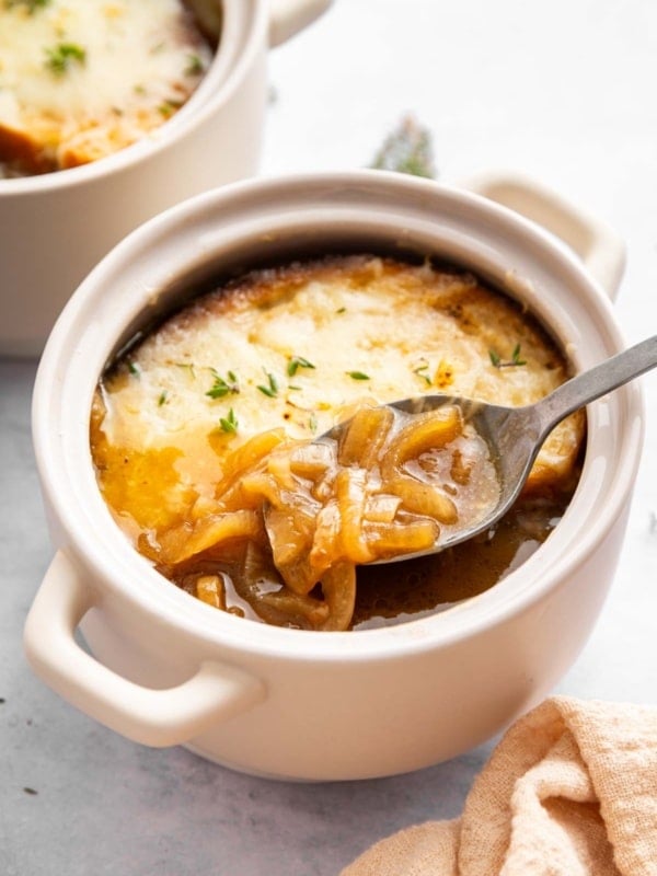 Bowl of French onion soup with spoon removing a scoop.