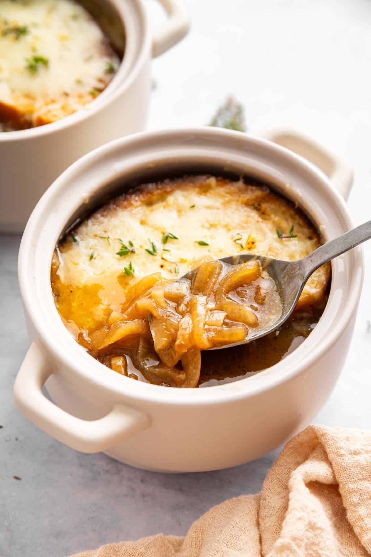 Bowl of French onion soup with spoon removing a scoop.