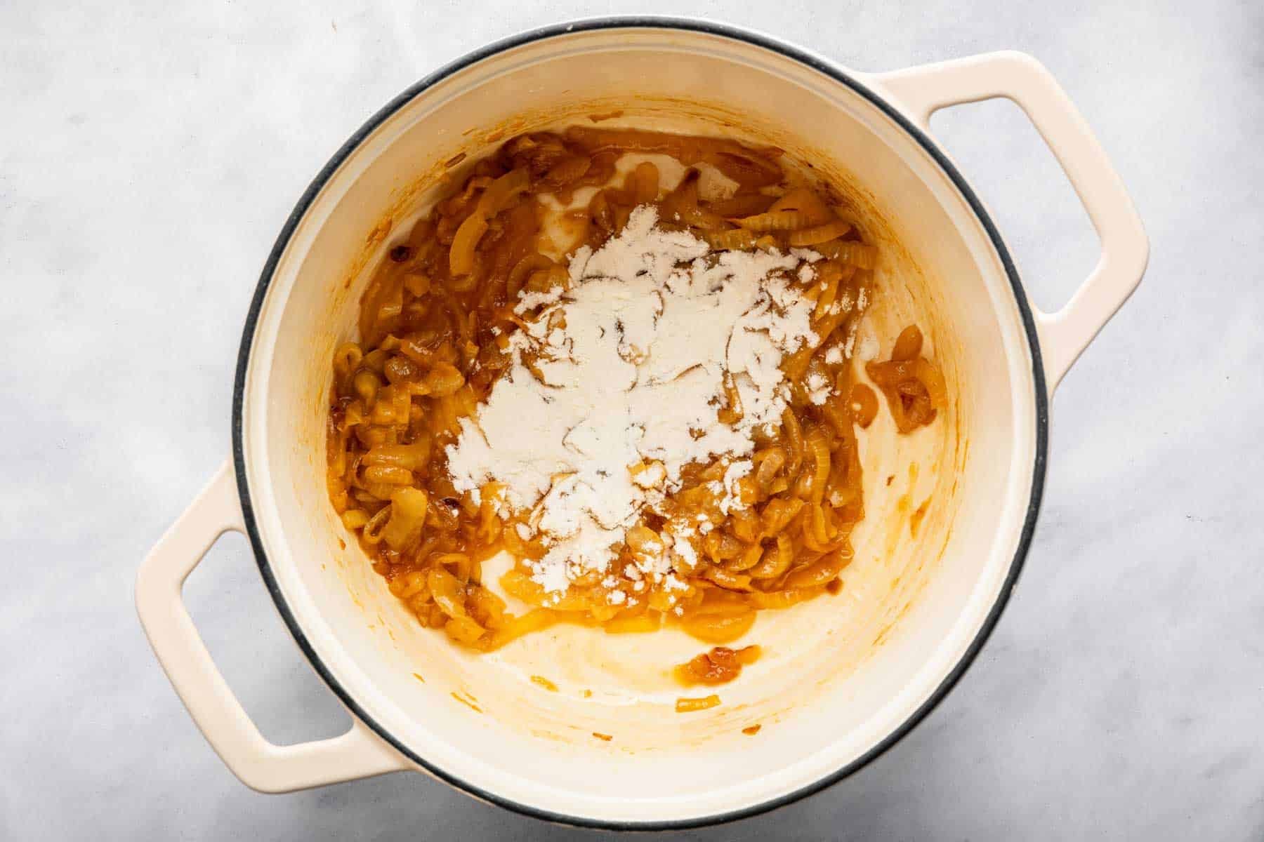 Flour sprinkled over caramelized vegetables in a pot.