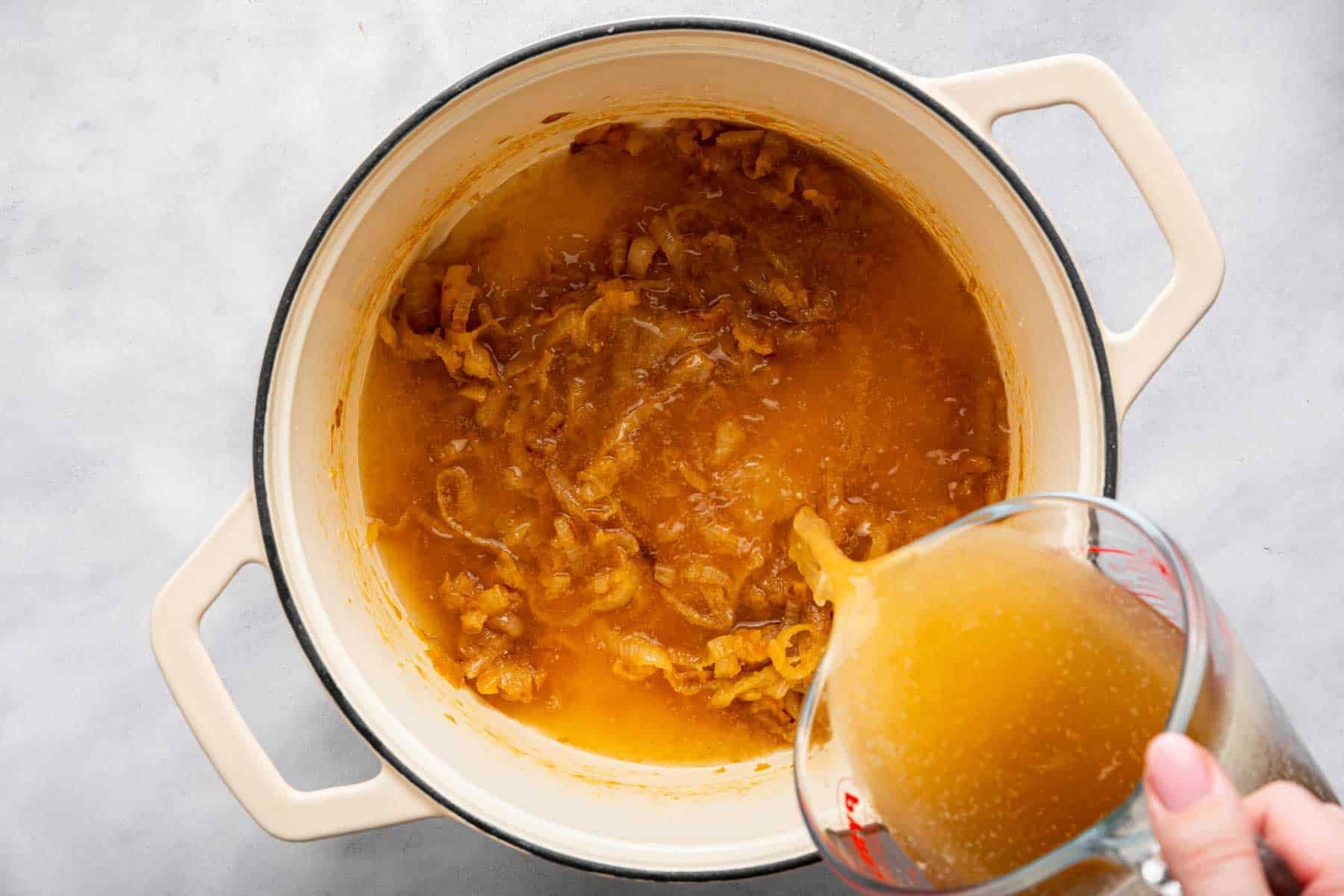 Hand pouring broth into white soup pot.