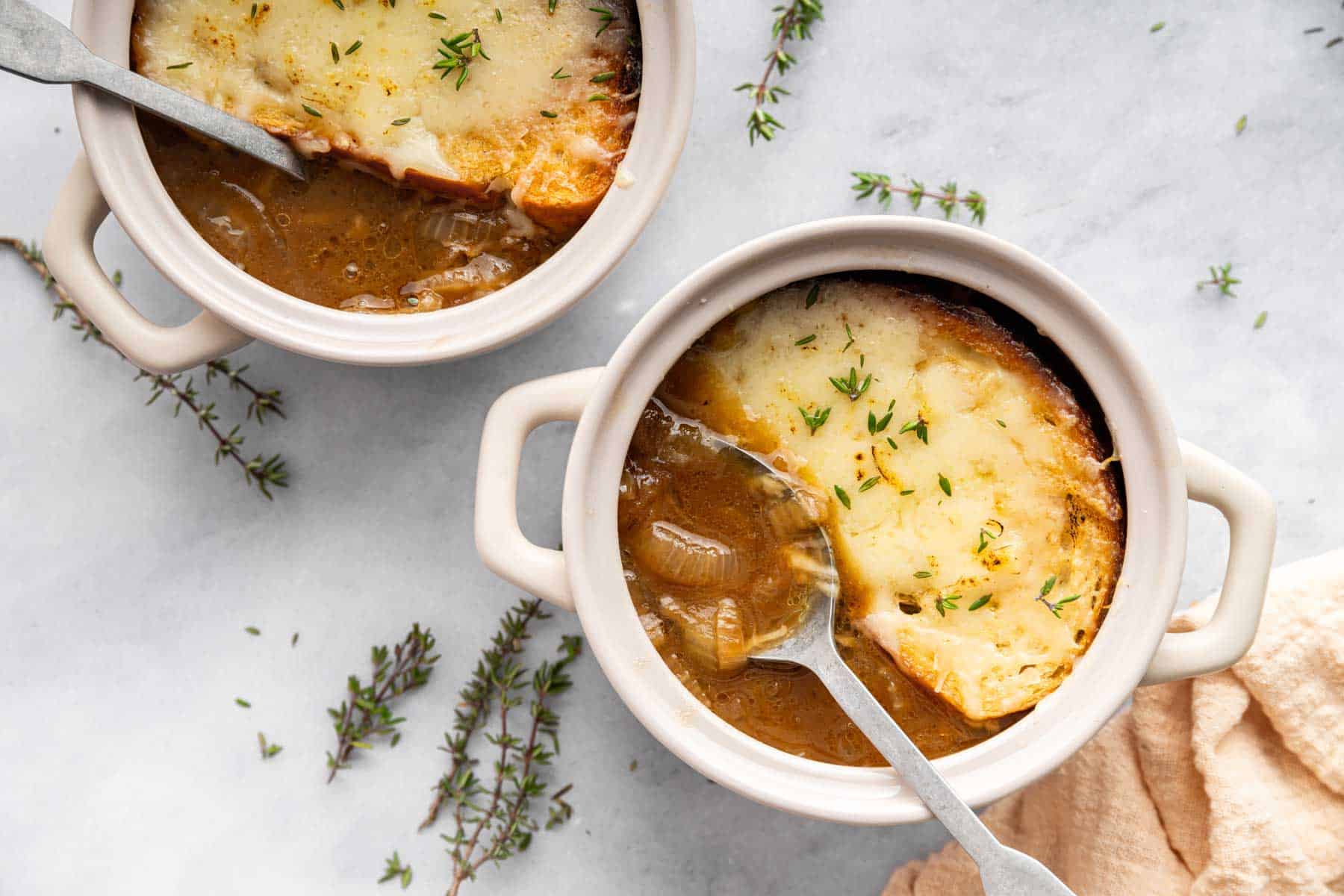 French onion soup for two in two bowls with spoon on side.