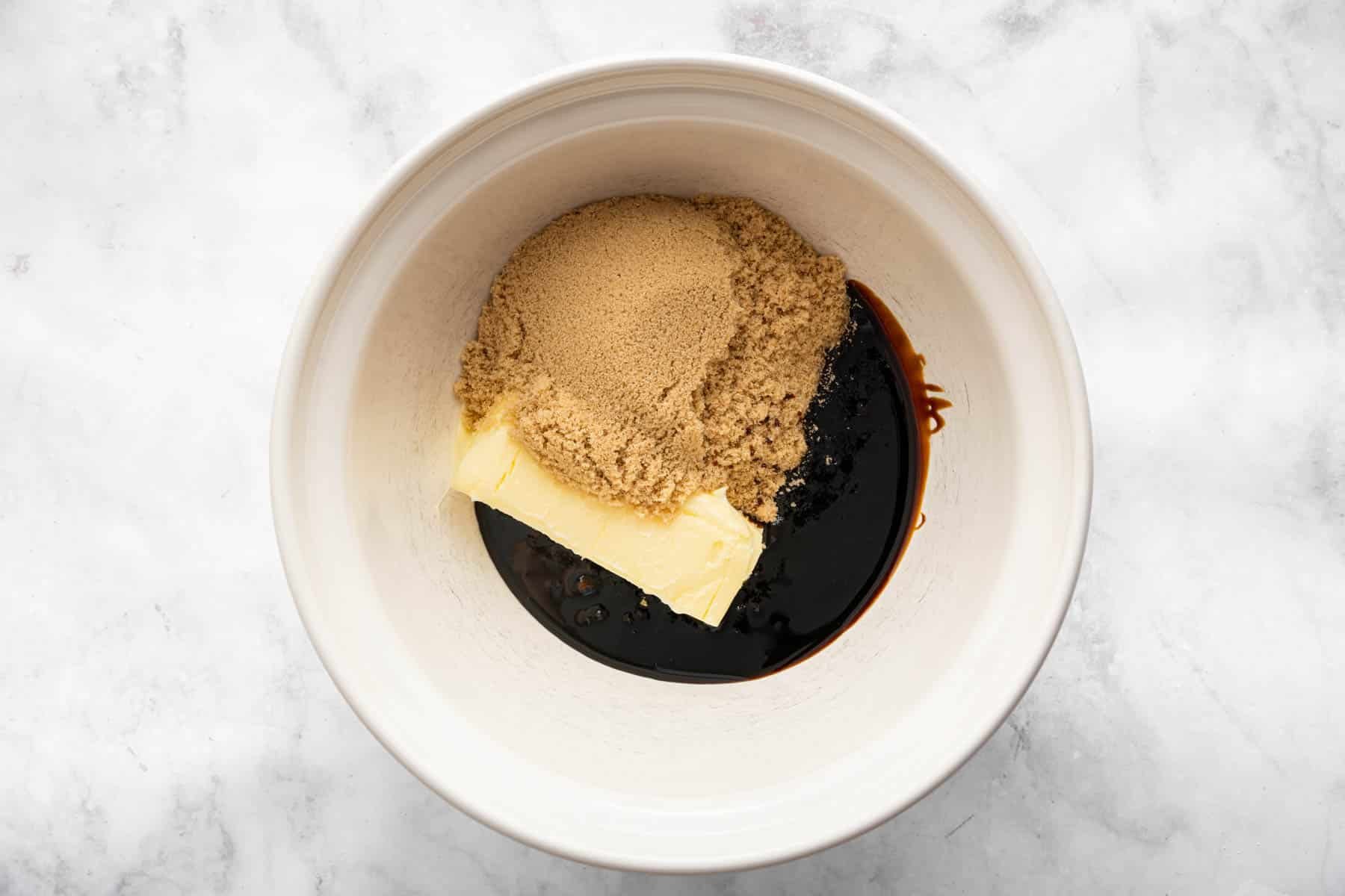 White bowl with butter, brown sugar, and molasses in it, unmixed.