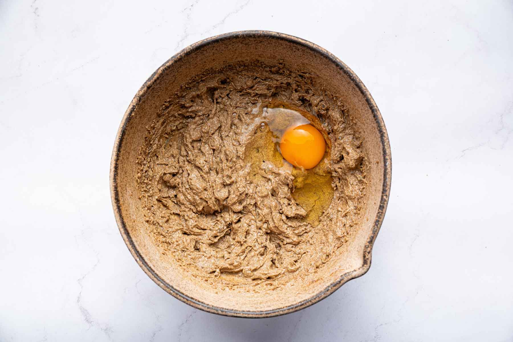 Brown bowl with brown batter with two raw eggs cracked into it.