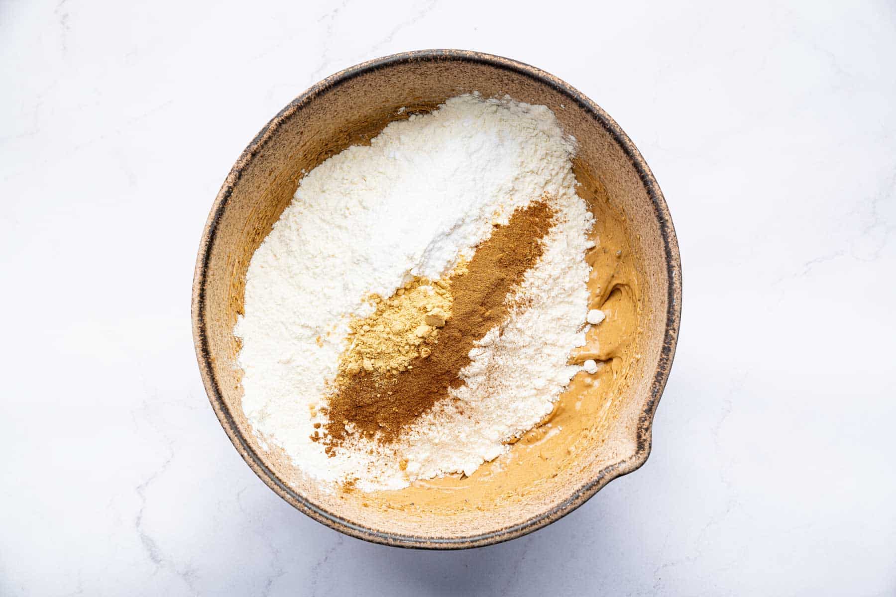 Flour and brown spices evenly distributed over batter in a bowl.