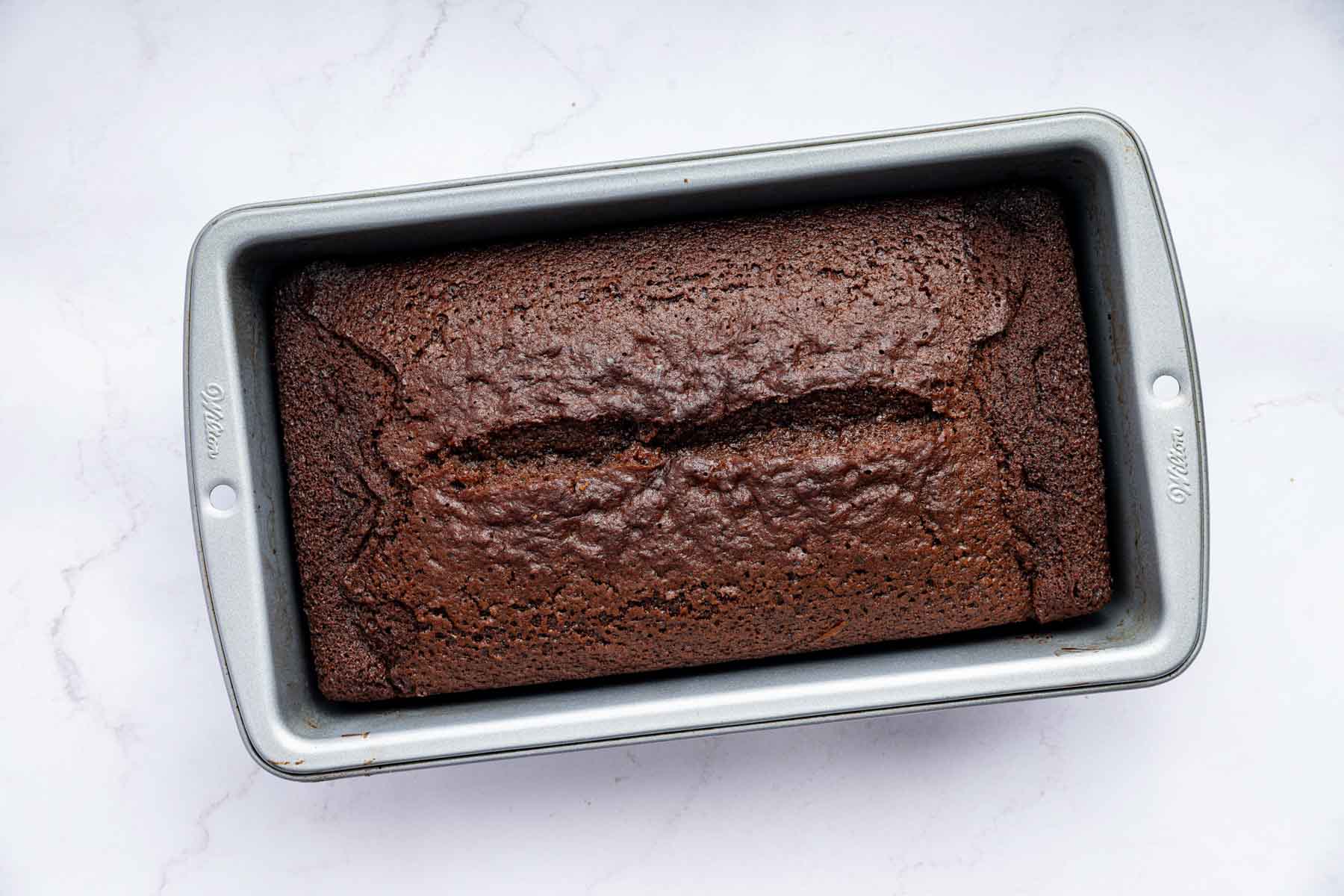 Baked gingerbread cake in a loaf pan with a crack down the middle.