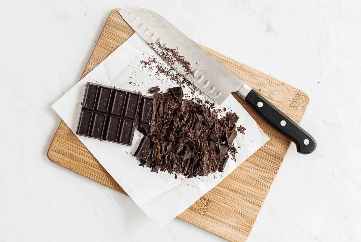 Bar of chocolate chopped on parchment paper and cutting board.