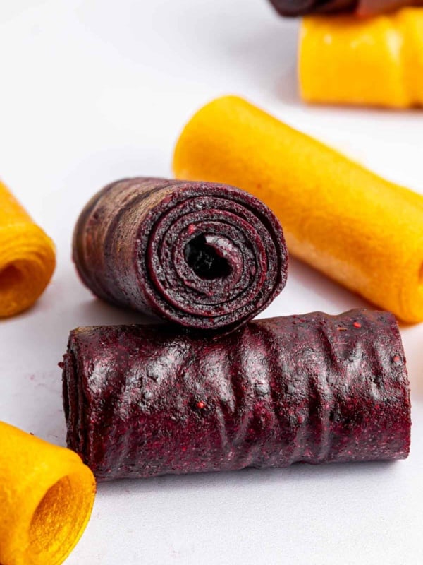 Purple and orange homemade fruit roll ups stacked on each other on counter.