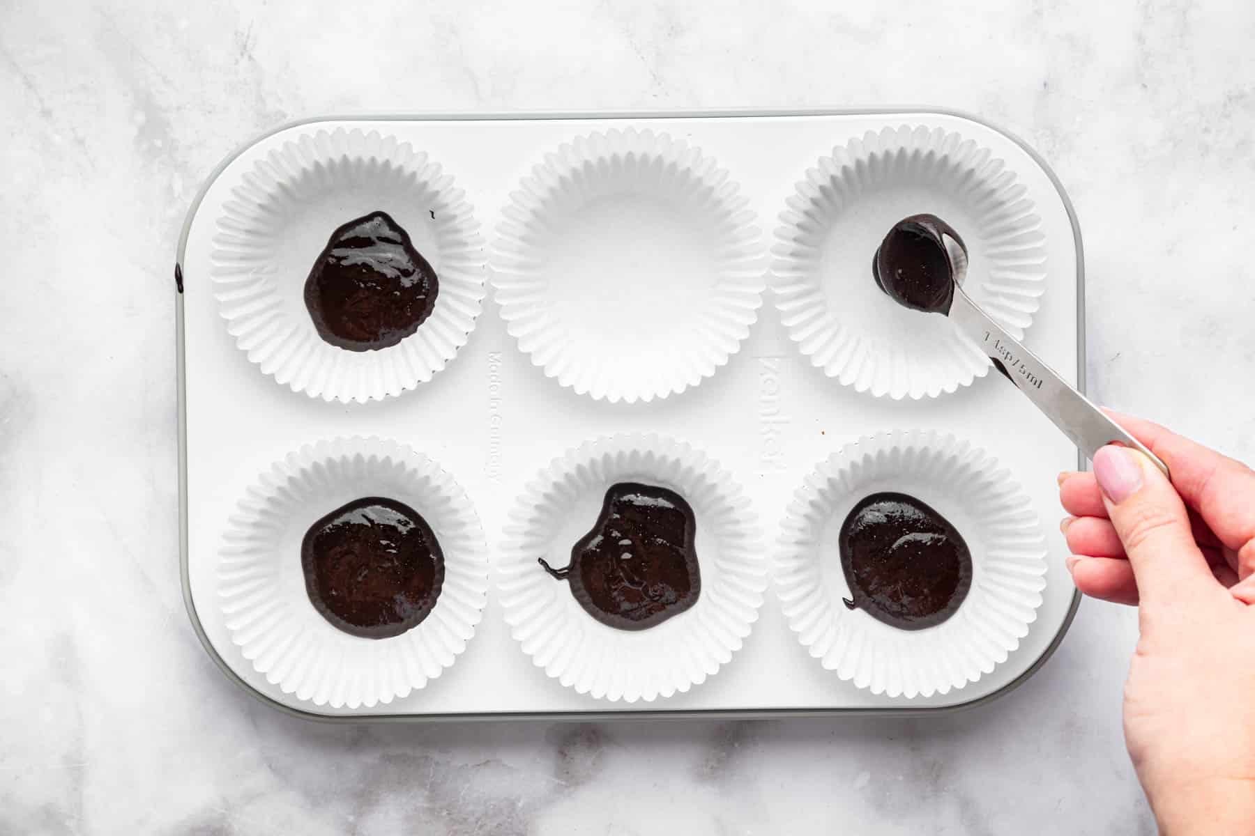 Hand pouring chocolate into muffin tin.