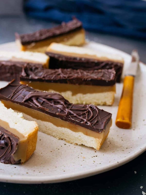 Homemade Twix bars on a plate with knife on side.
