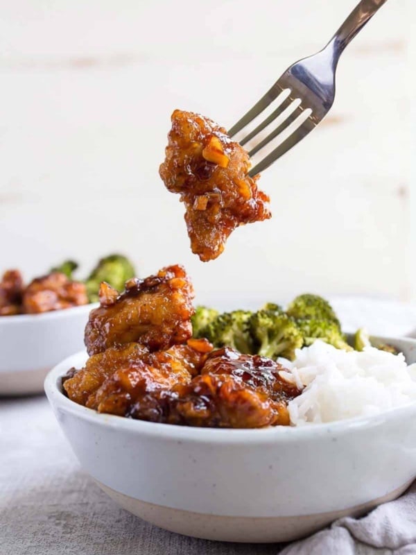 Fork removing a golden brown piece of food from a bowl with rice and broccoli.