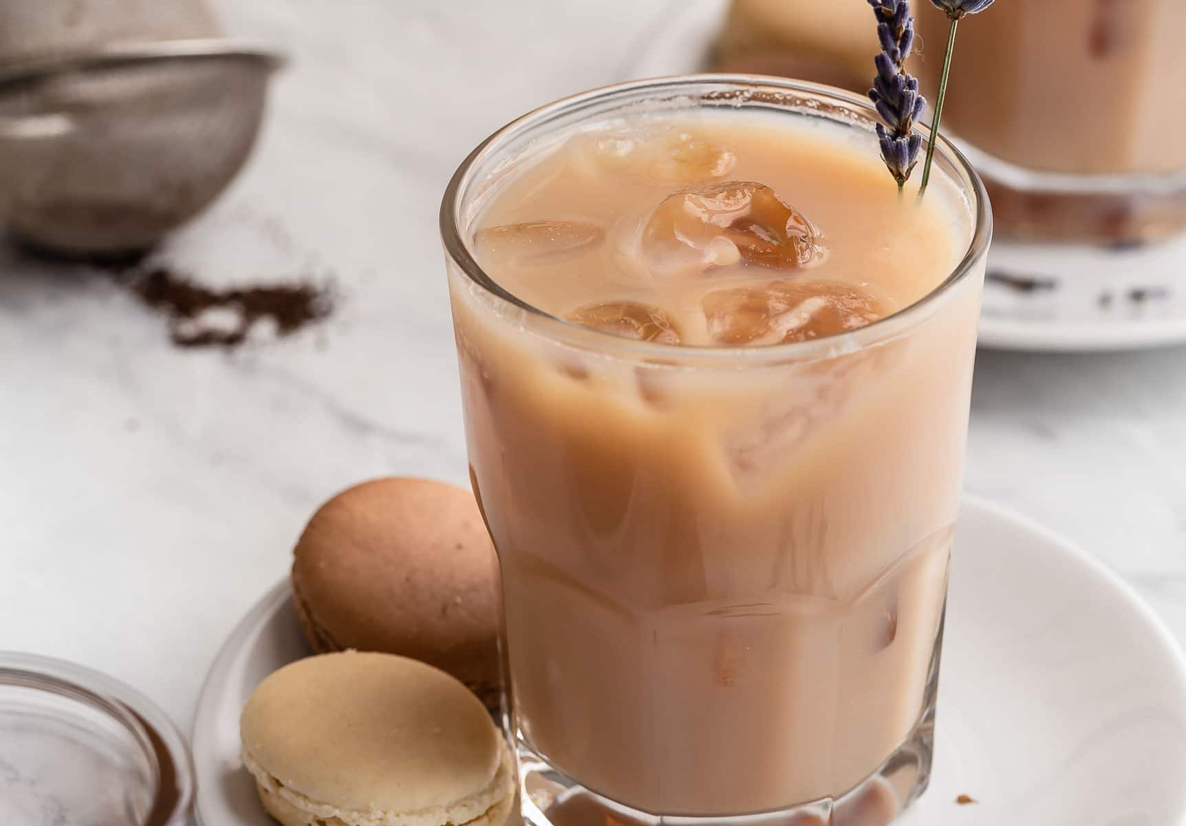 Two milky iced tea glasses with lavender sprig garnish.