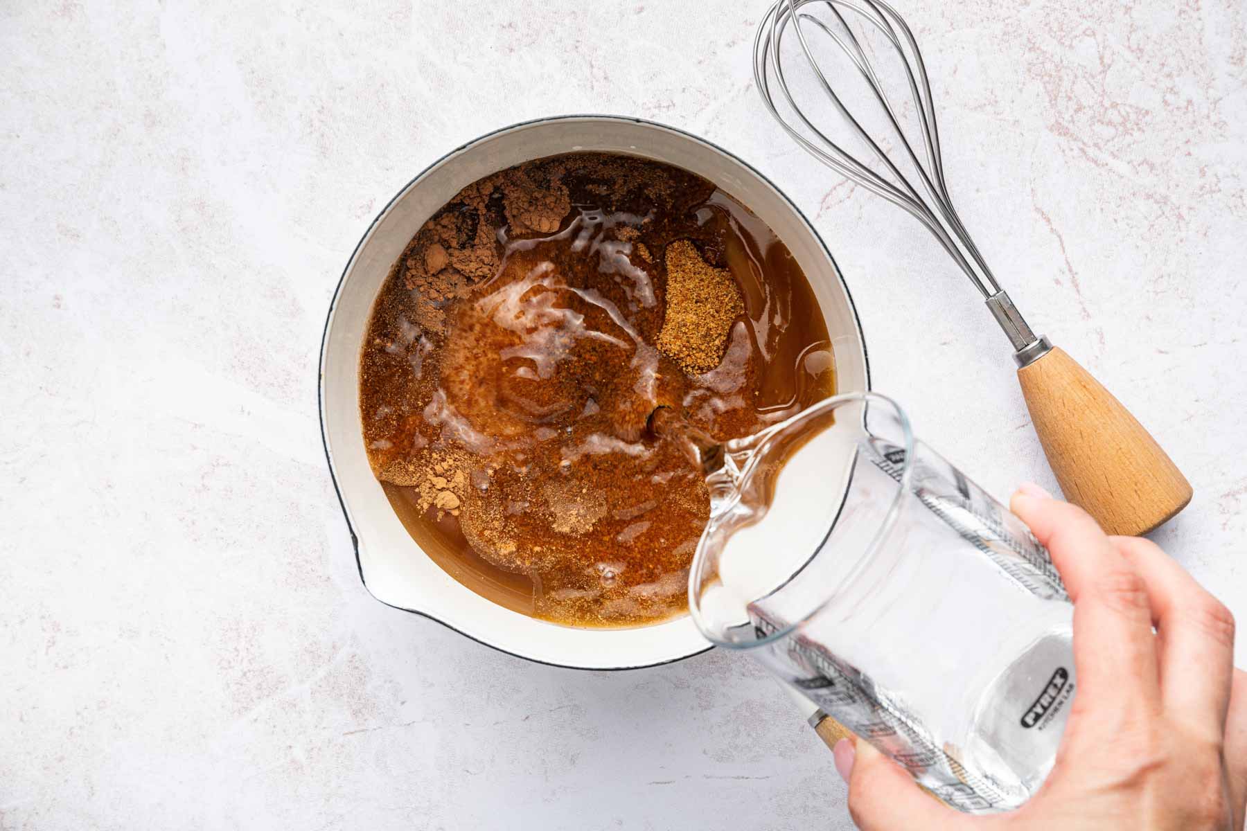 Hand pouring water into small saucepan with cocoa powder and honey.