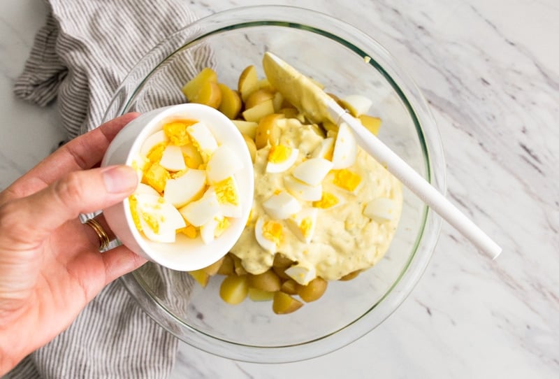Hand pouring diced hard boiled eggs into bowl.