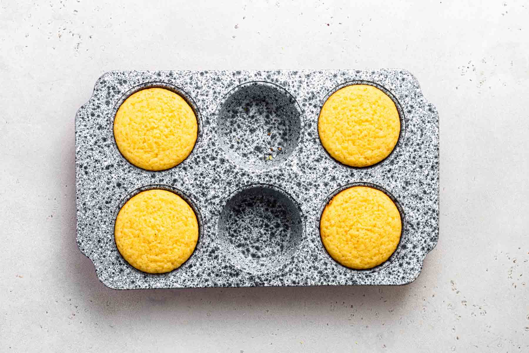 Four lemon cupcakes in a muffin pan, after baking.