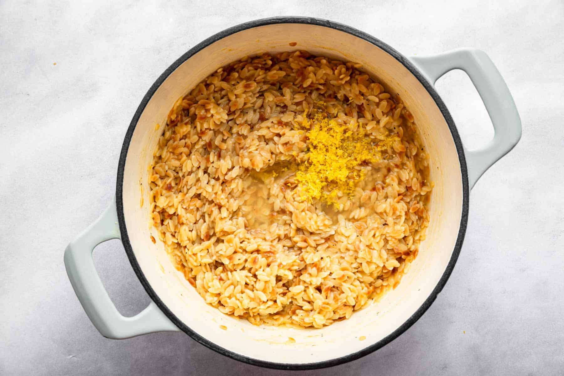 Lemon zest on top of pasta in a white pot.
