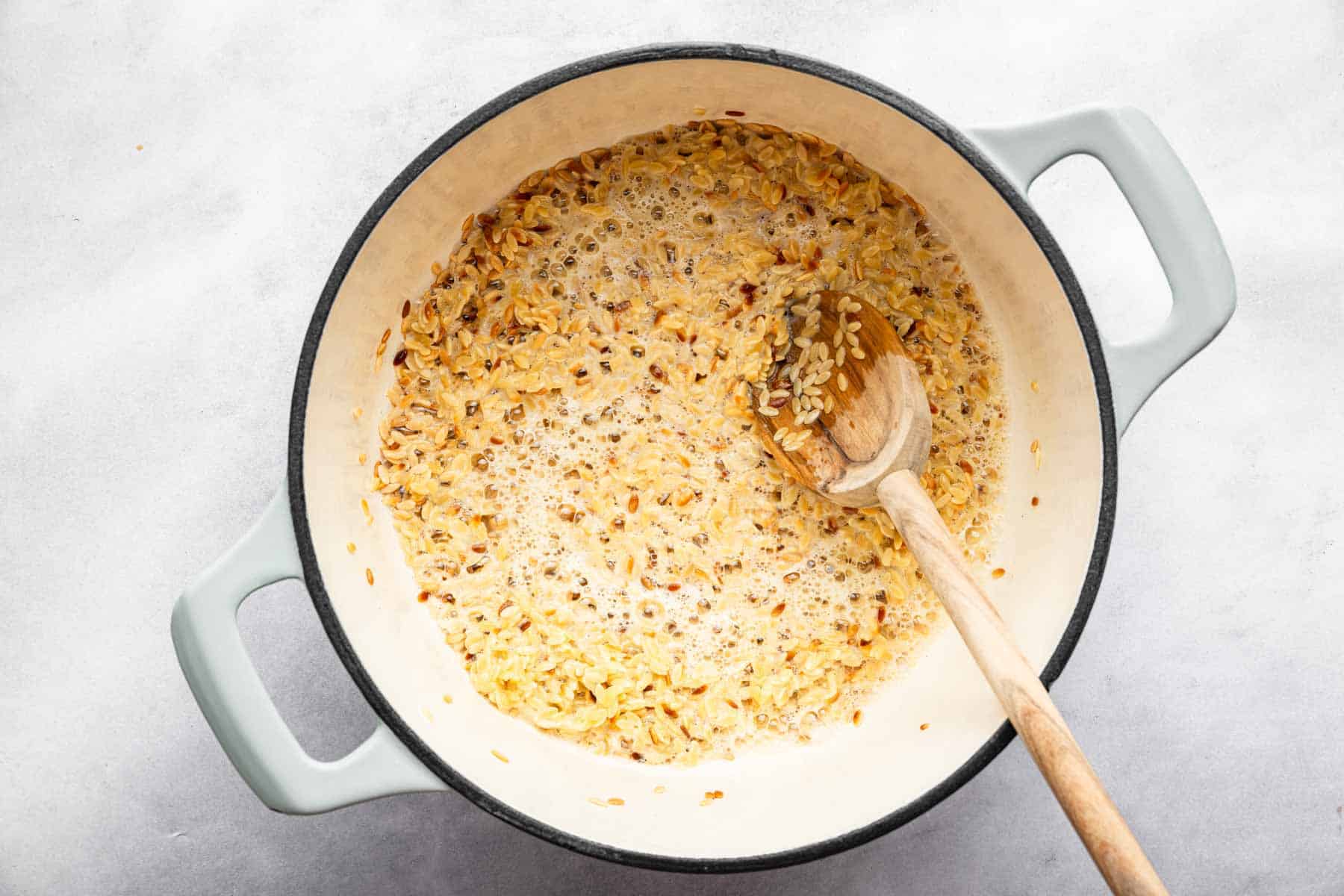 White dutch oven with pasta sizzling and wooden spoon.
