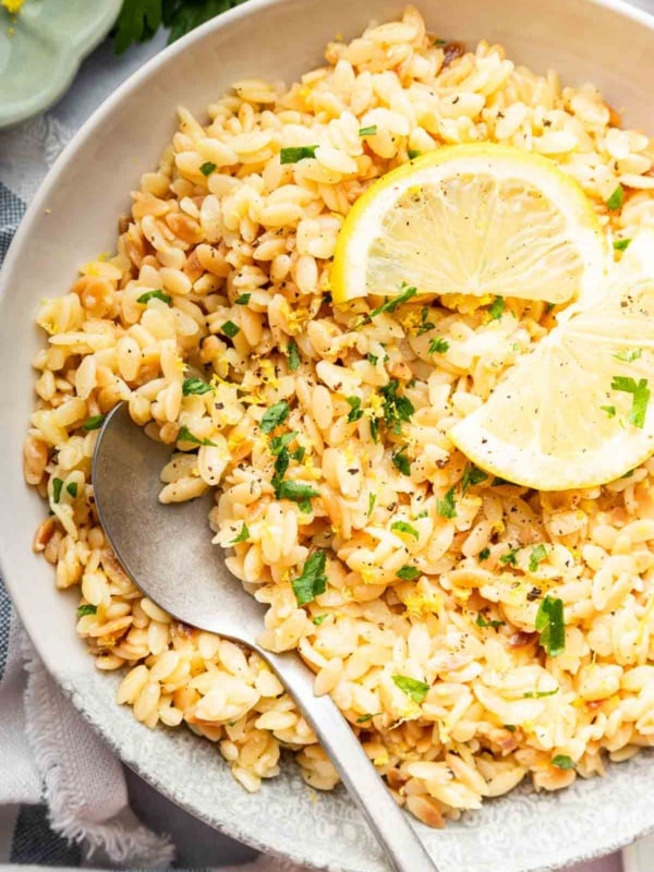 Bowl of lemon orzo garnished with lemon slices and a spoon.