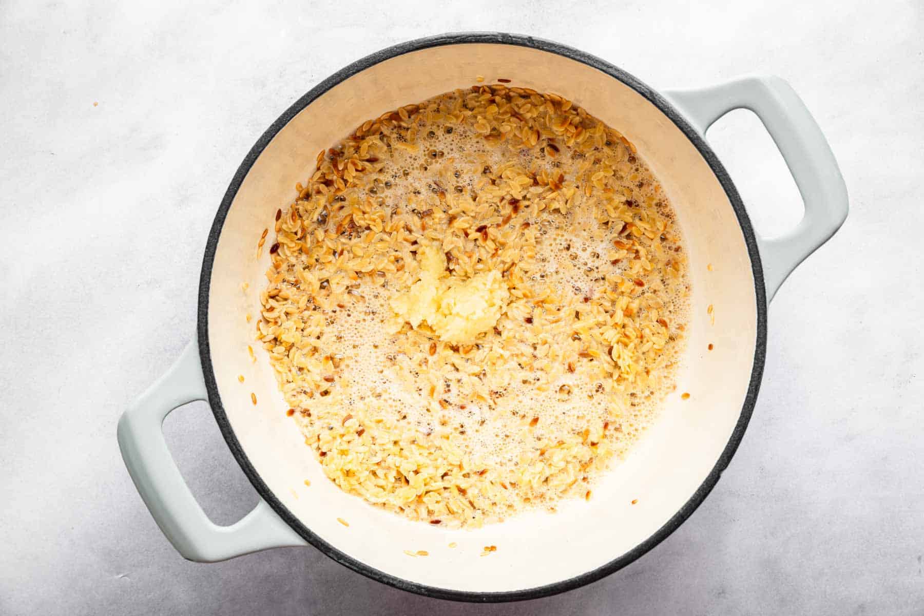Minced garlic in a pan with sizzling pasta.