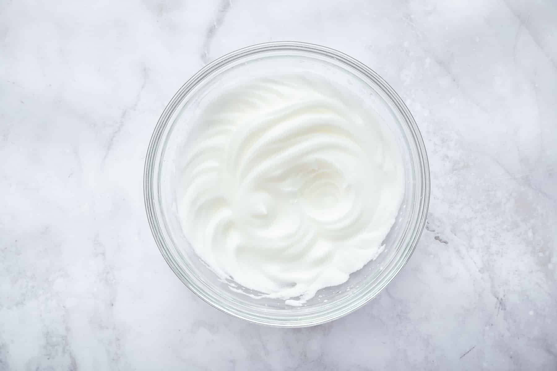 Freshly whipped raw egg white in a clear bowl.
