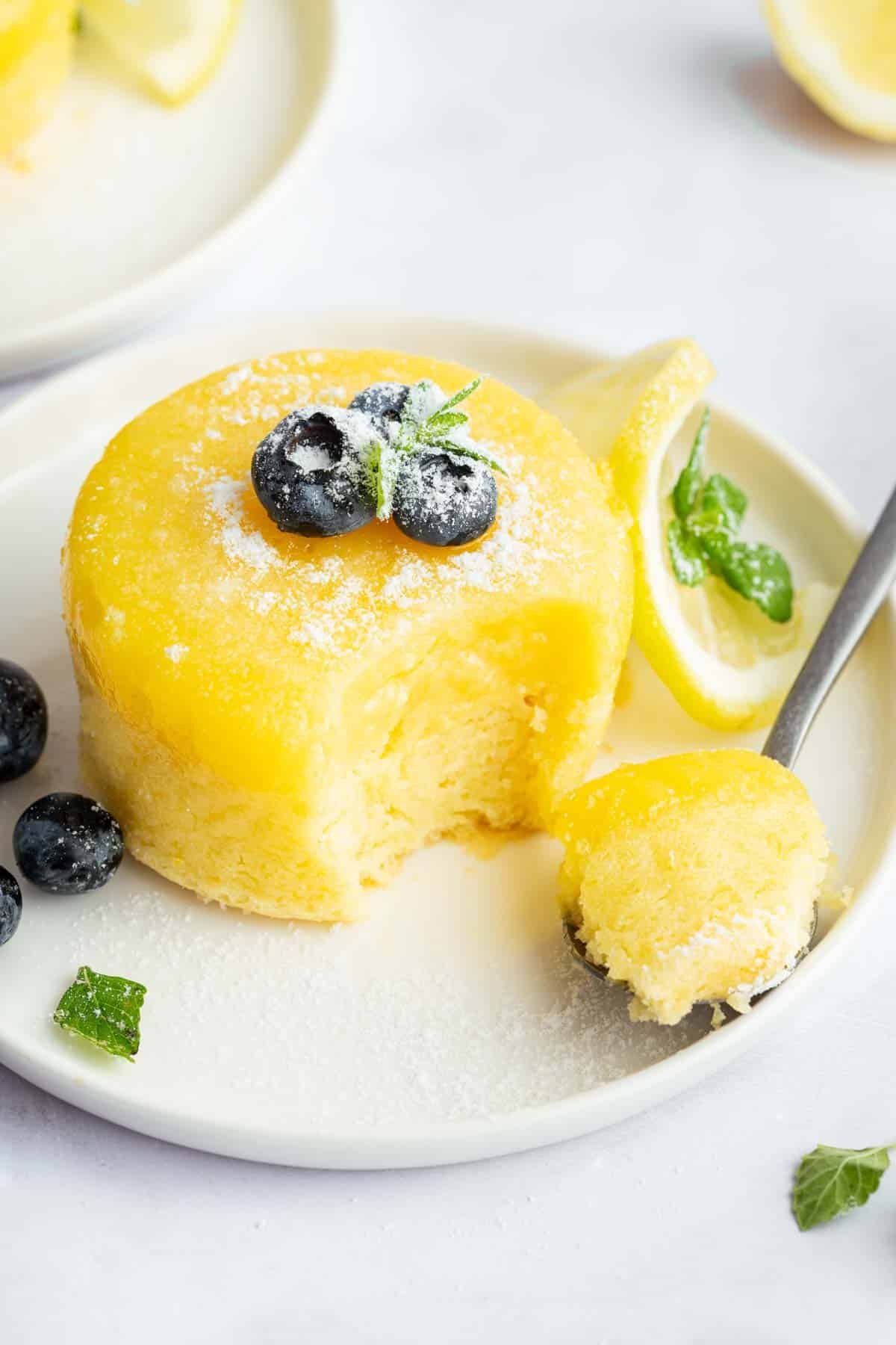 lemon-pudding-cake Bright yellow lemon pudding cake on a plate garnished with blueberries.